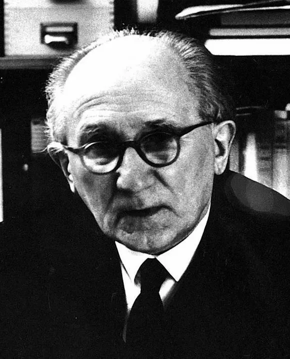 Romano Guardini in höherem Alter an seinem Schreibtisch vor Bücherregalen
